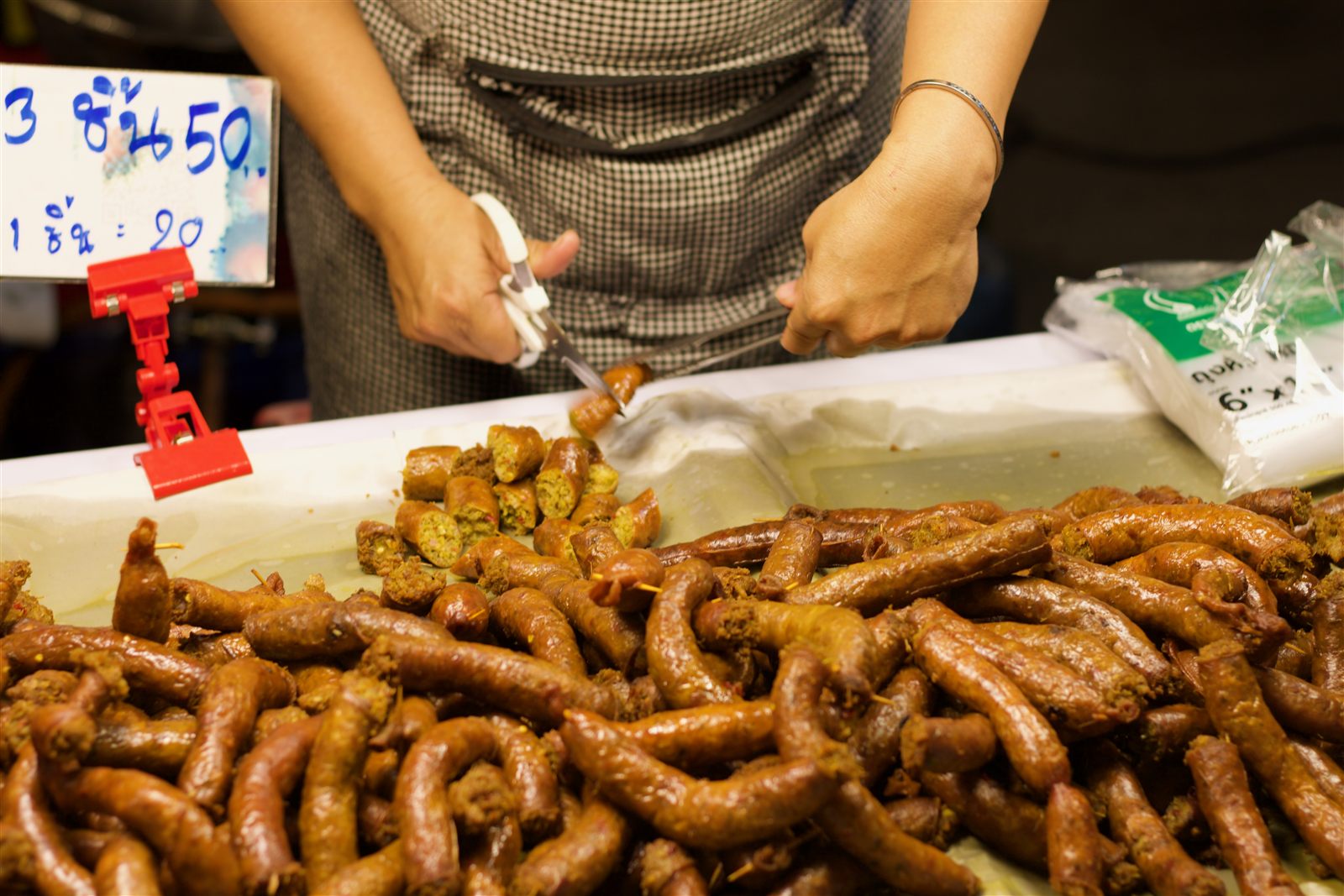 Street Food & Tuk-Tuk — a vendor cutting grilled Chiang Mai sausage at a night market stall