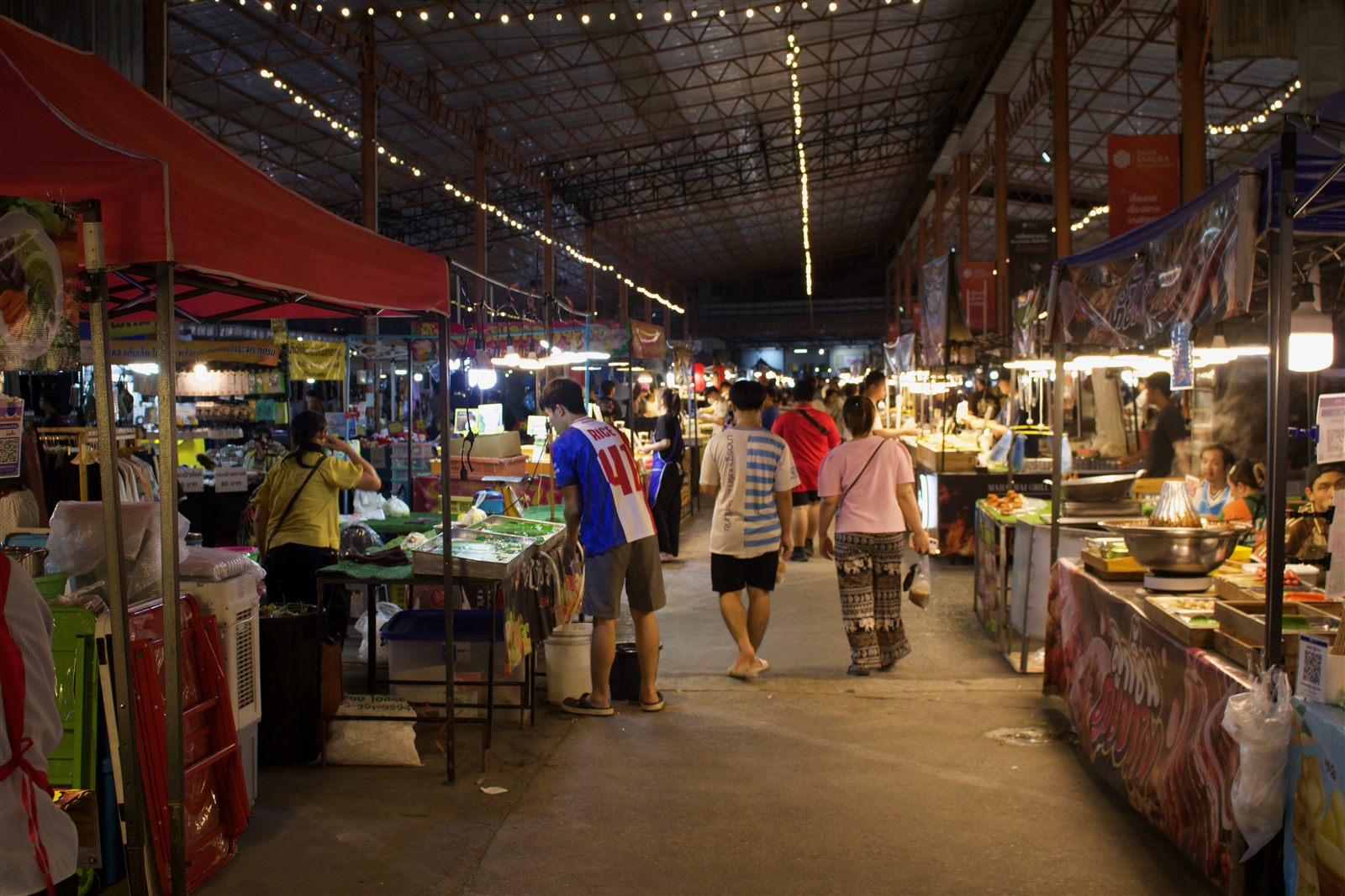 Street Food & Tuk-Tuk — shoppers walking through the covered night market, stalls lit up on both sides